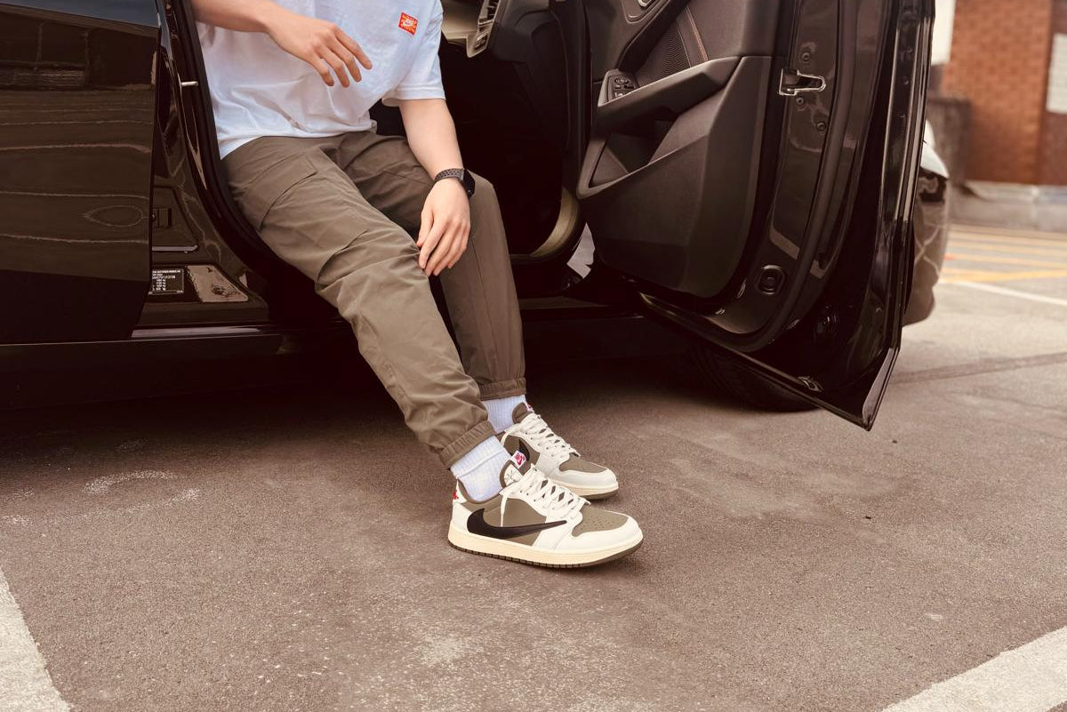 Lifestyle image of replica designer trainers UK worn on foot, featuring Jordan 1 Retro Low OG SP Reverse Olive with black and olive panelling, white midsole, and red branding – ideal for buyers seeking designer trainer dupes and high quality replica trainers with streetwear appeal